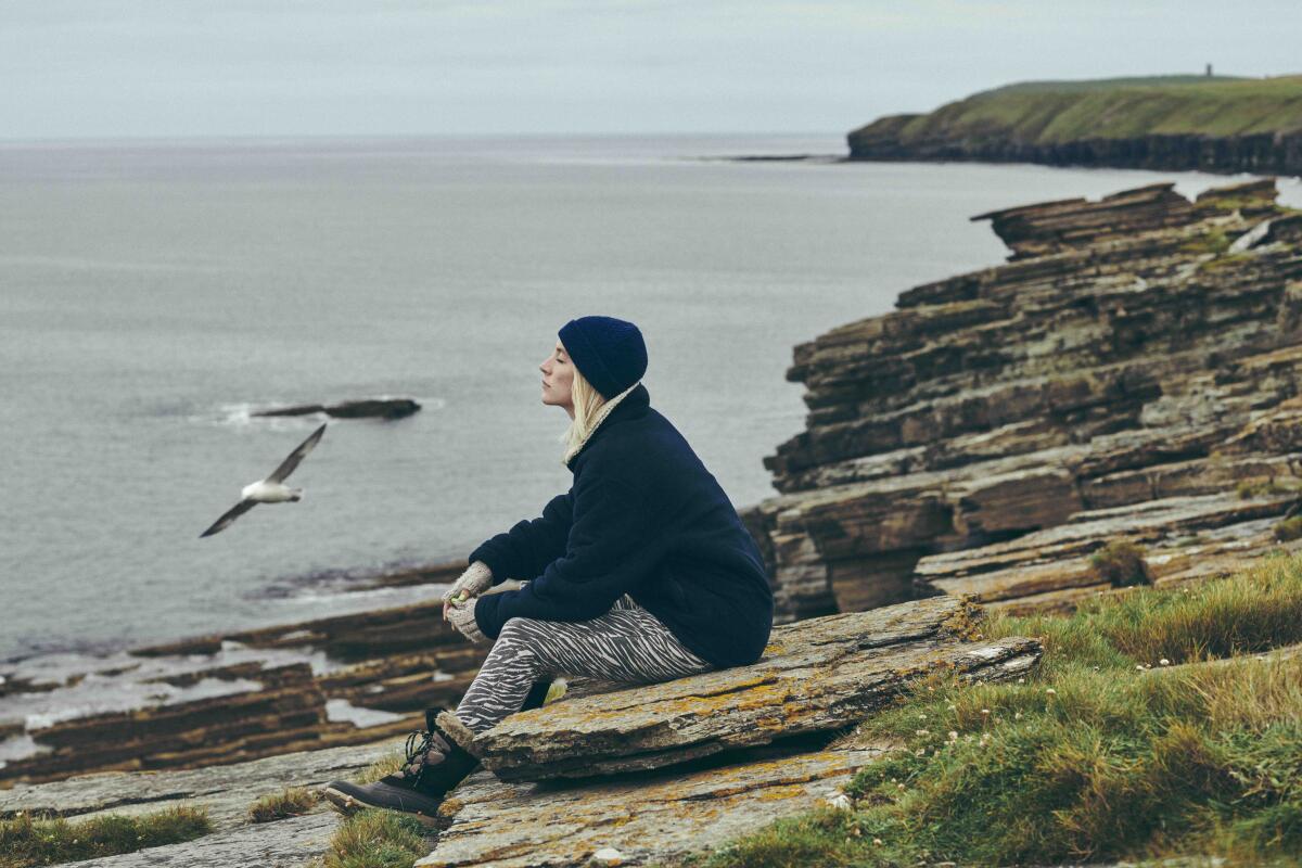 A woman sits at a body of water, her eyes closed.