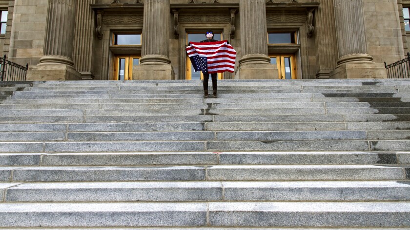 A student holding a U.S. flag upside down stands atop the steps at the Idaho Capitol Building.