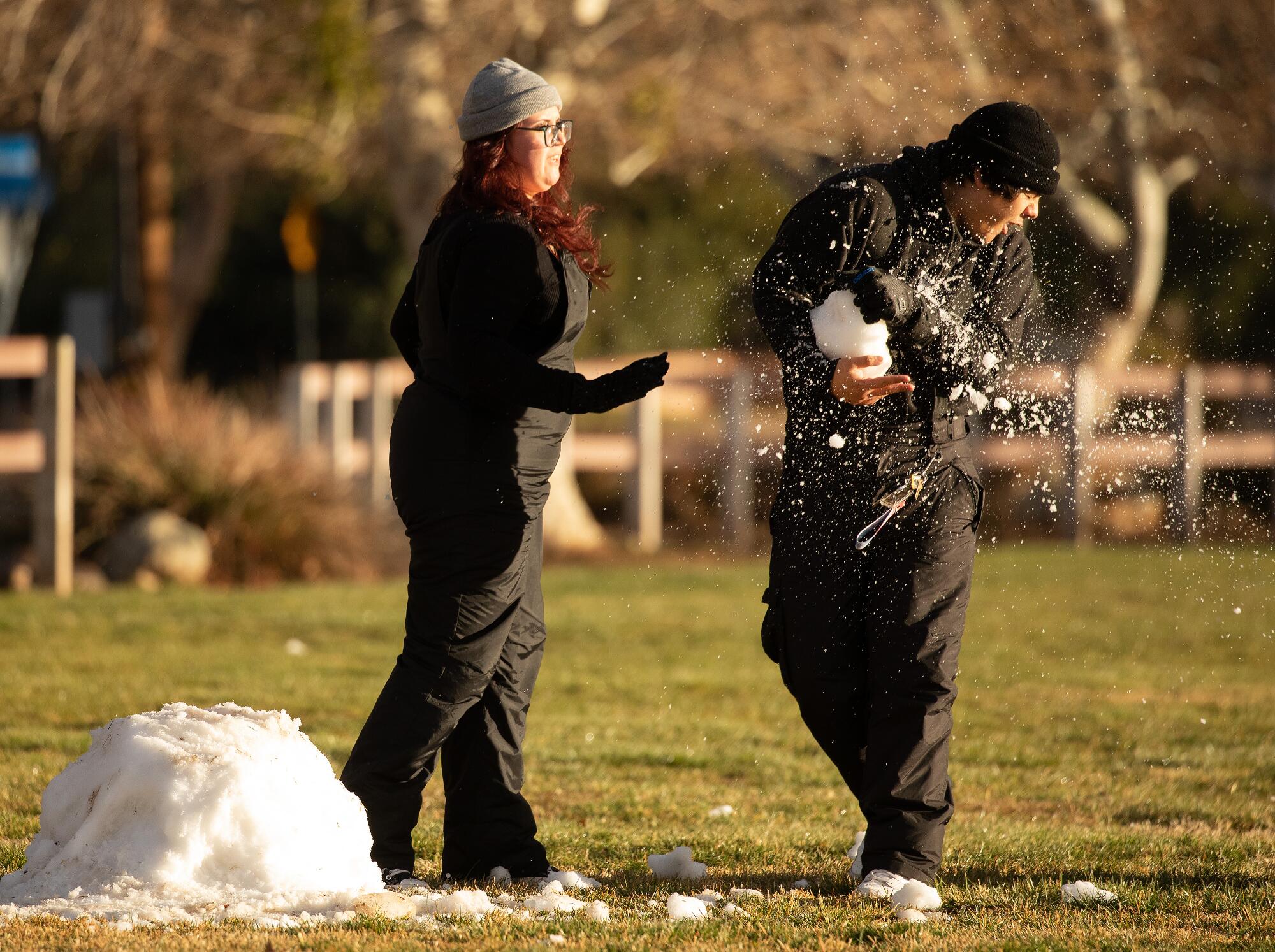 Carmen Meza lands a shot during a snowball fight with her boyfriend, using a small remaining pile of snow on a grassy field.