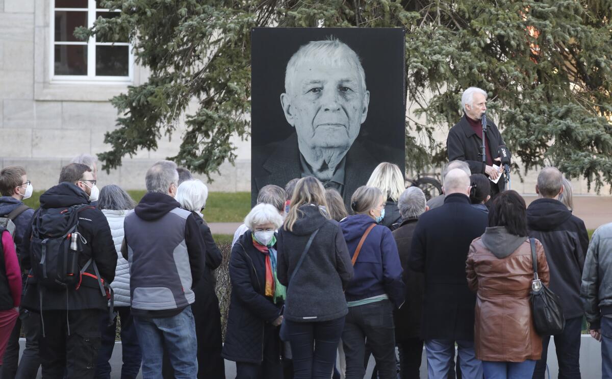 People stand outdoors in front of a large photo of a man 