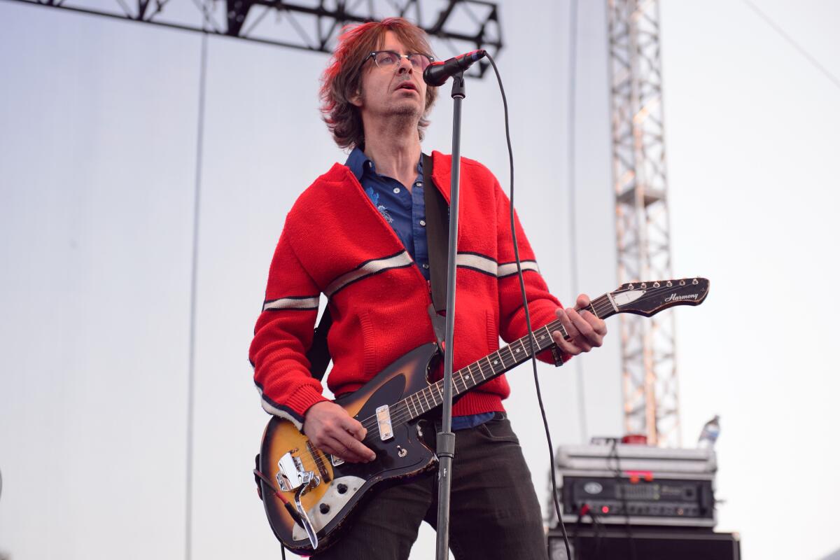 A man playing electric guitar onstage on a red jacket