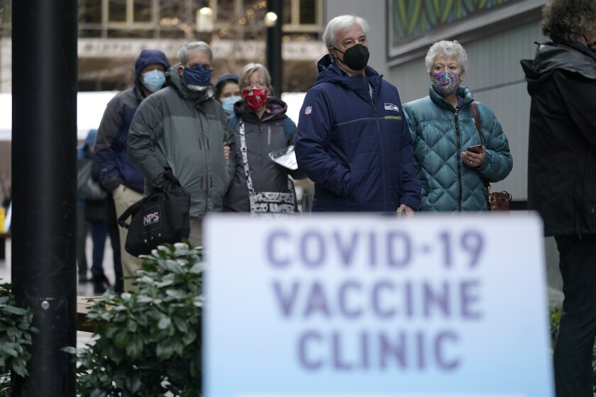 FILE - In this an. 24, 2021, file photo, people stand near a sign as they wait in line to receive the first of two doses of the Pfizer vaccine for COVID-19 at a one-day vaccination clinic set up in an Amazon.com facility in Seattle and operated by Virginia Mason Franciscan Health. Scientists say it's still too early to predict the future of the coronavirus, but many doubt it will ever go away entirely. (AP Photo/Ted S. Warren, File)