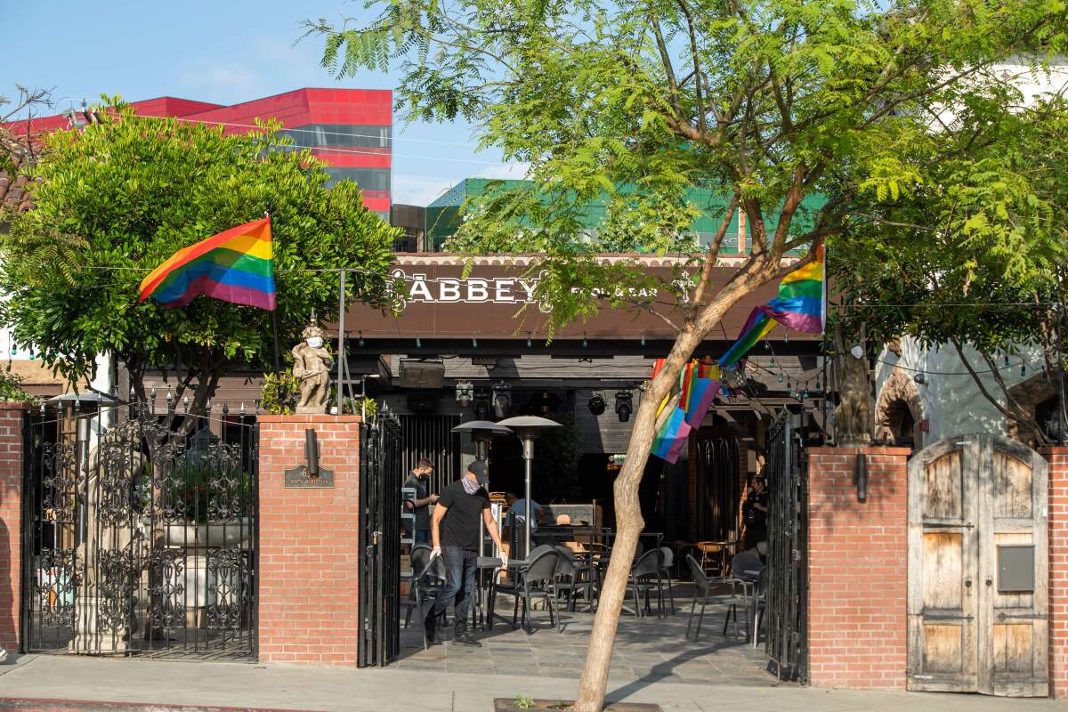 The exterior of a restaurant with tables on a patio and trees in front.