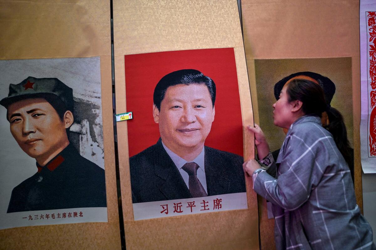 A seller holds a portrait of Xi Jinping next to one of Mao Zedong 