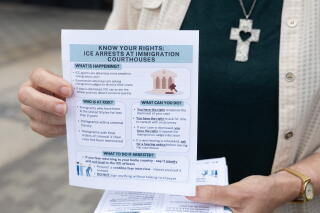 A woman wearing a cross holds a pamphlet instructing immigrants on their legal rights.