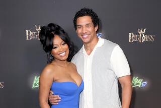 Keke Palmer in a strapless blue dress posing alongside a man in a white shirt with grey panels and beige pants
