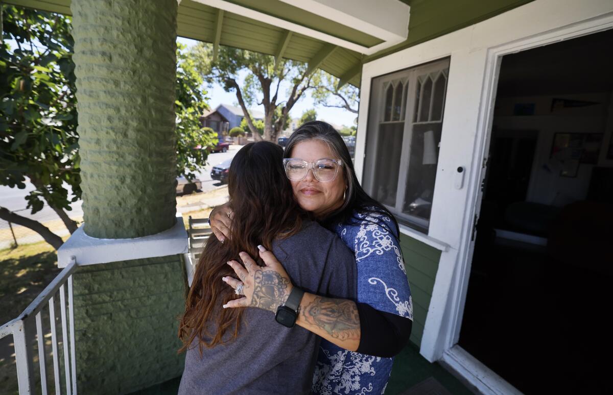 Two women embrace on a porch.