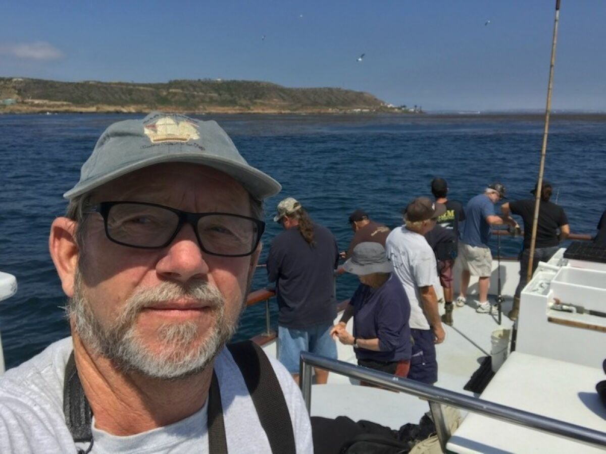 A man takes a selfie on a fishing boat with people standing in the background.