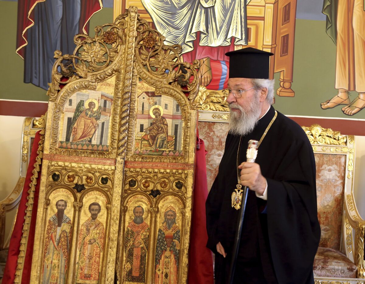 The leader of Cyprus Orthodox Church, Archbishop Chrysostomos II stands next to a pair of ornate, gilded doors that guard the altar of a church, at the Archbishopric in the capital Nicosia, on Thursday, Sept. 16, 2021 . The 18th century doors that were looted from the church of Saint Anastasios in the breakaway north of the ethnically divided island nation were repatriated from a Japanese art college after a long legal battle.(AP Photo/Philippos Christou)