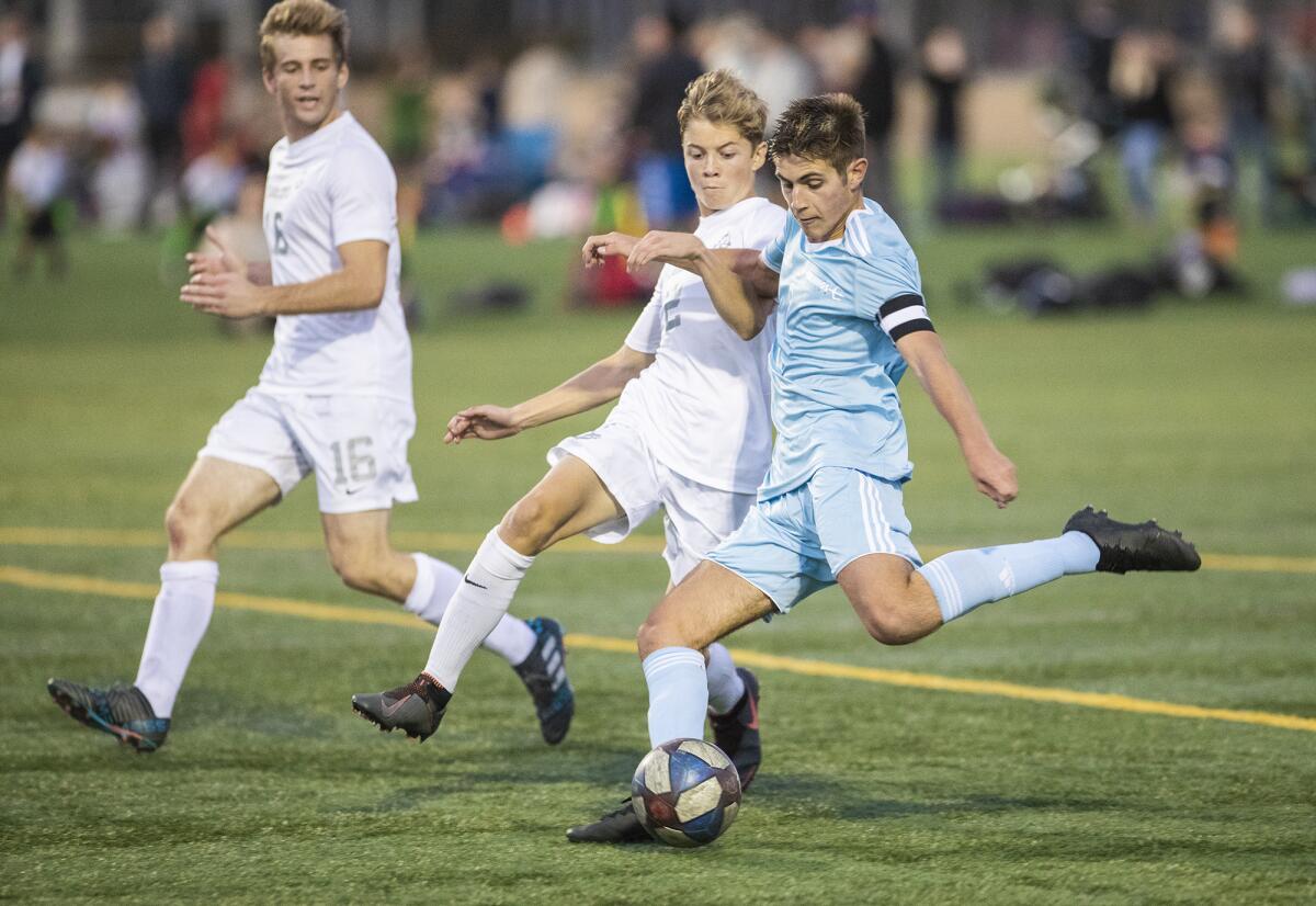 Corona del Mar's Aidan Holmes shoots and scores while being defended by Newport Harbor's Nicolas Del Villar, center, during a Battle of the Bay match at Bonita Creek Park on Friday.