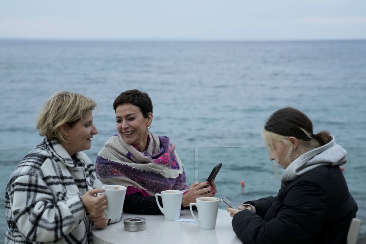 Three women drink coffee at a seaside restaurant 