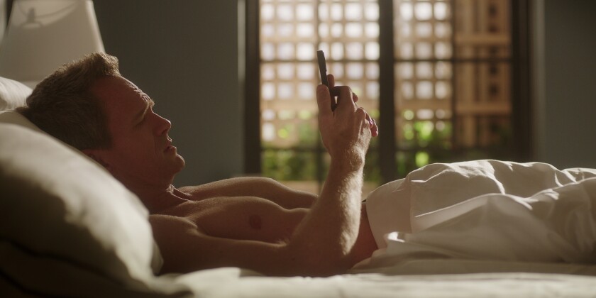 A shirtless man laying in bed looking at his phone
