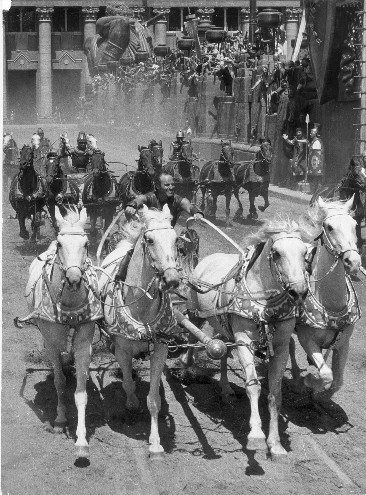 Charlton Heston as Ben-Hur driving a chariot pulled by four white horses.