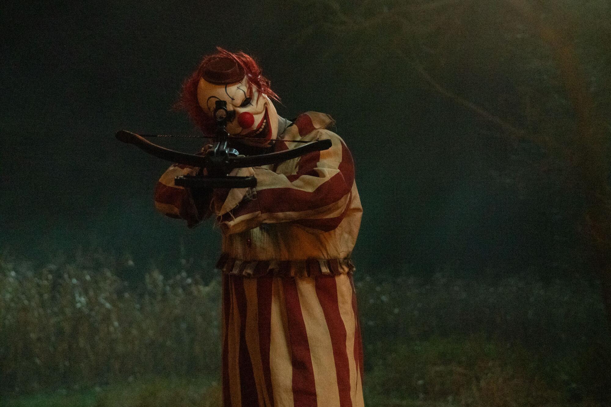 A clown in a cornfield wields a weapon.