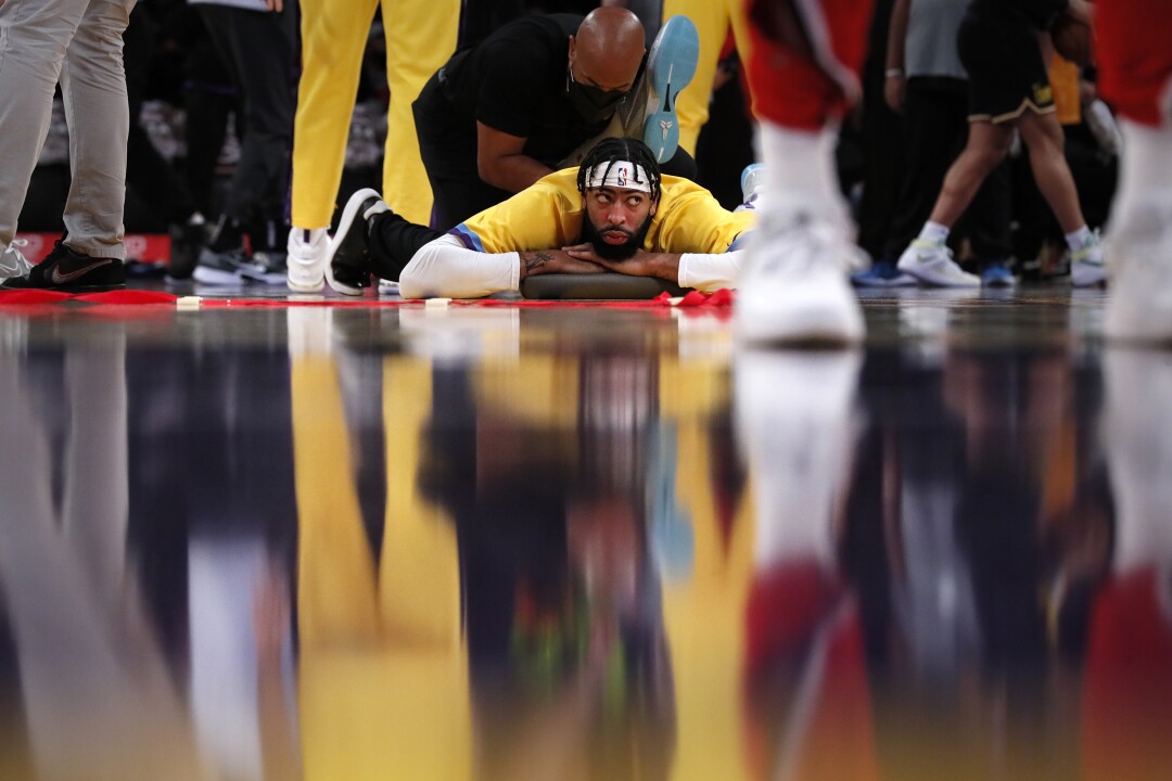 Anthony Davis lies on his stomach on the court as a trainer treats him