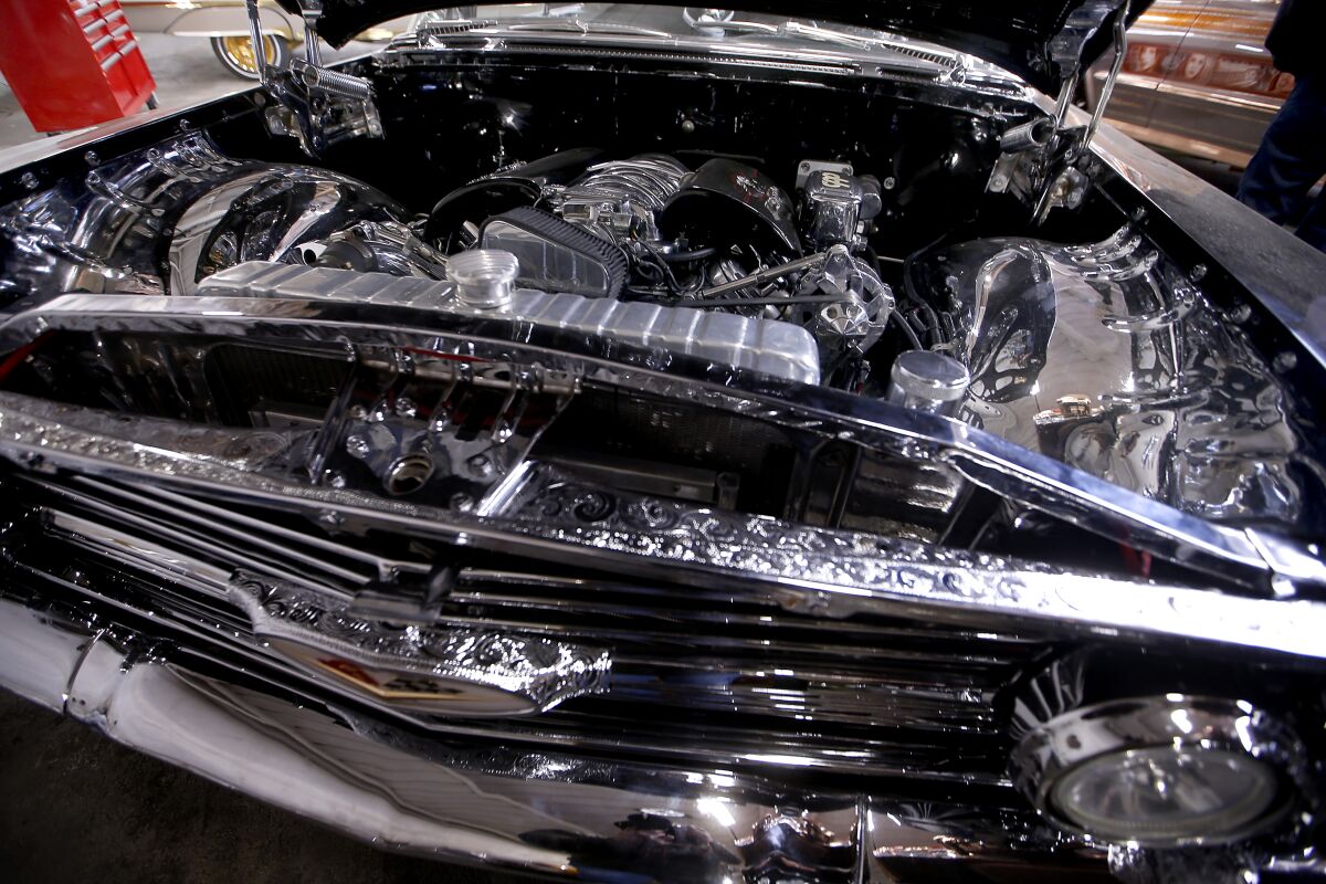 An open hood reveals a chrome-plated engine in a Chevrolet Impala. 