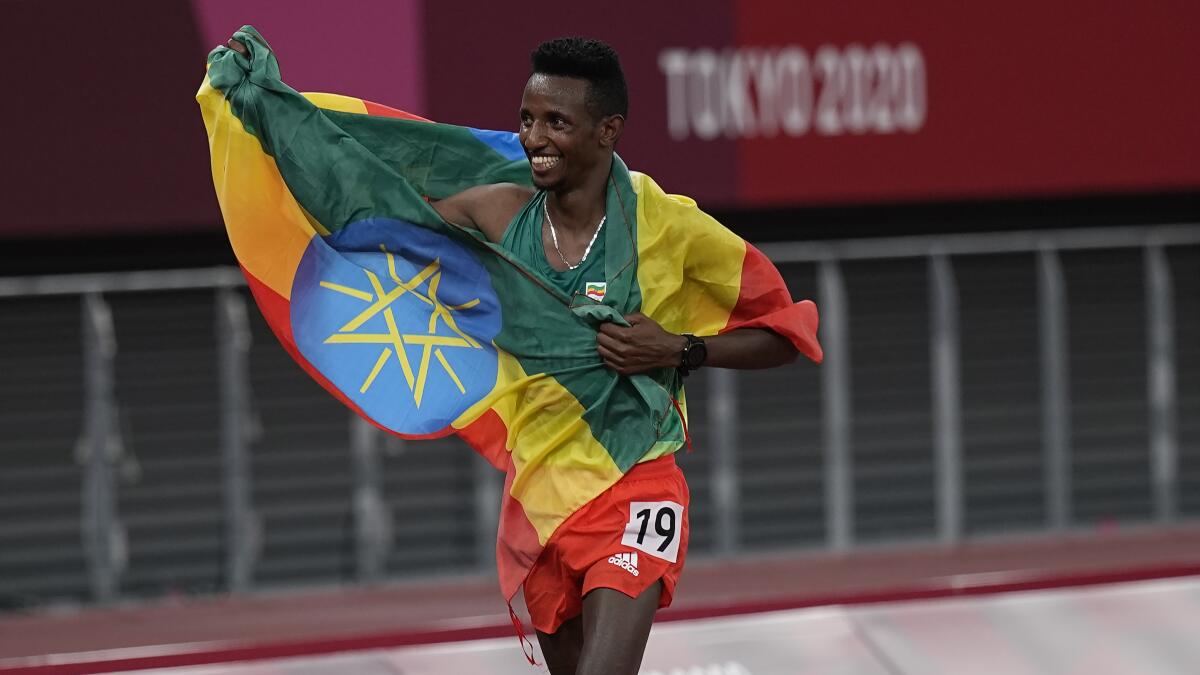 Selemon Barega, draped in the Ethiopian flag, smiles broadly as he walks on the track after his victory