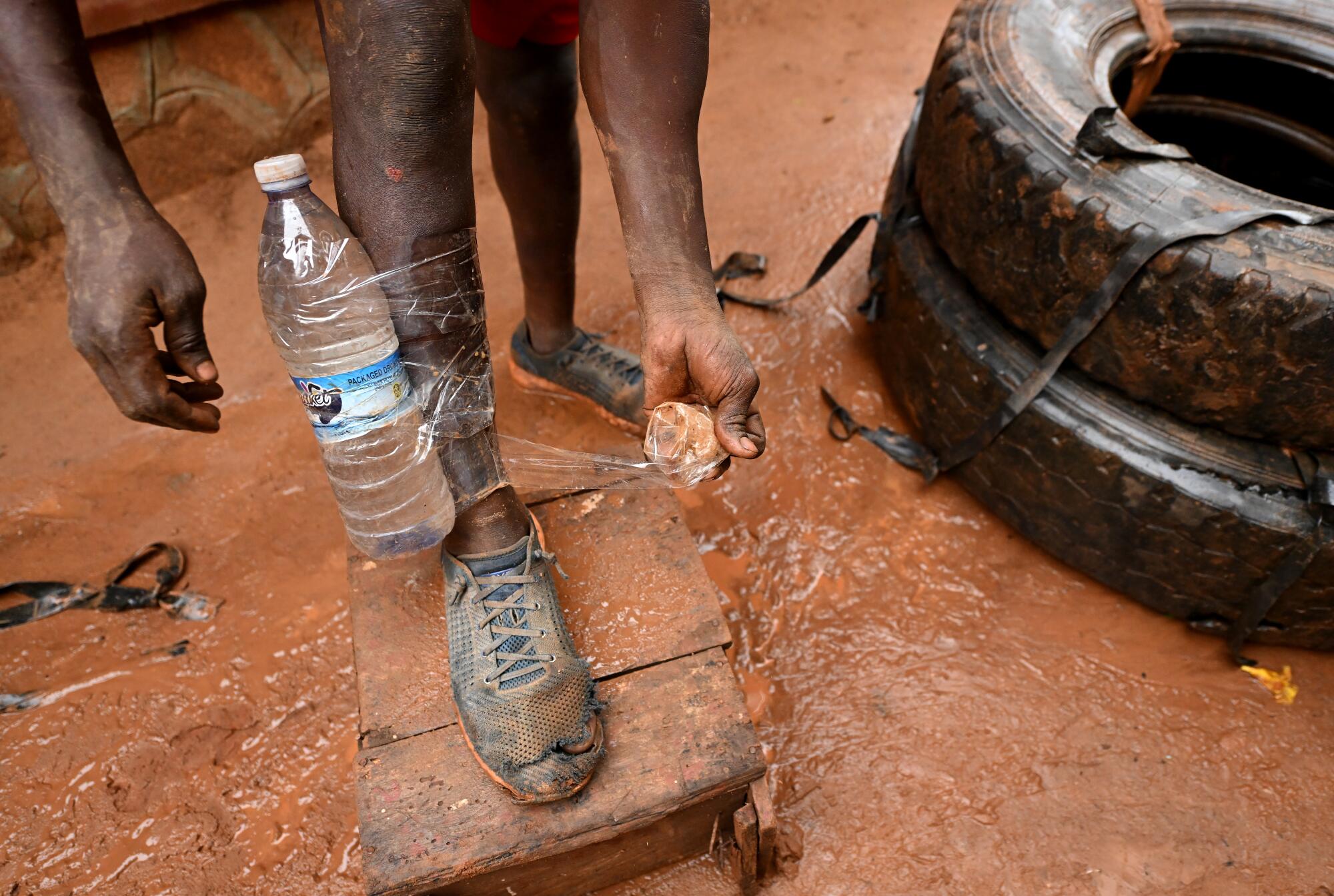 Dennis Kasumba ties a water bottle to his leg during his daily morning workout outside his home.