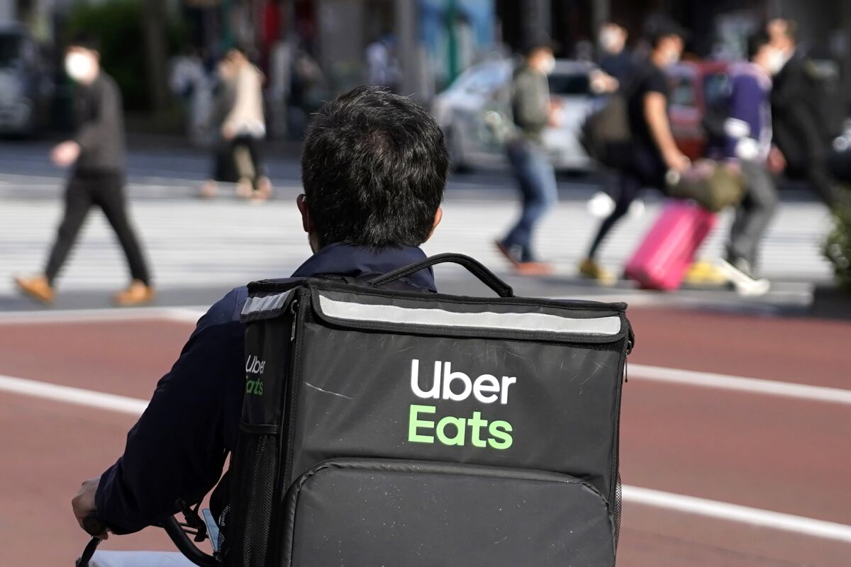 FILE - In this April 28, 2021, file photo, an Uber Eats delivery person rides a bicycle through the Shinjuku district in Tokyo, Japan. Uber’s ride-hailing service is regaining most of the momentum that it lost during the pandemic. At the same time, its delivery service is still growing at a torrid pace, indicating that some homebound habits may be here to stay, even though people are going out again. (AP Photo/Shuji Kajiyama, File)