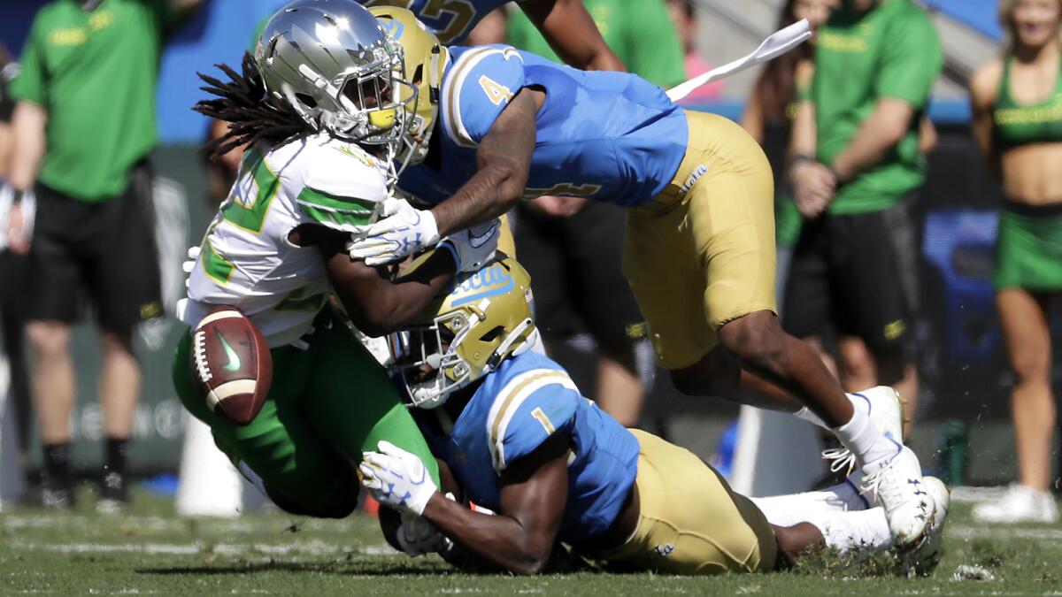Oregon running back Darian Felix fumbles as he is hit by UCLA defenders Darnay Holmes (1) and Jaleel Wadood (4) during the first half Saturday at the Rose Bowl.
