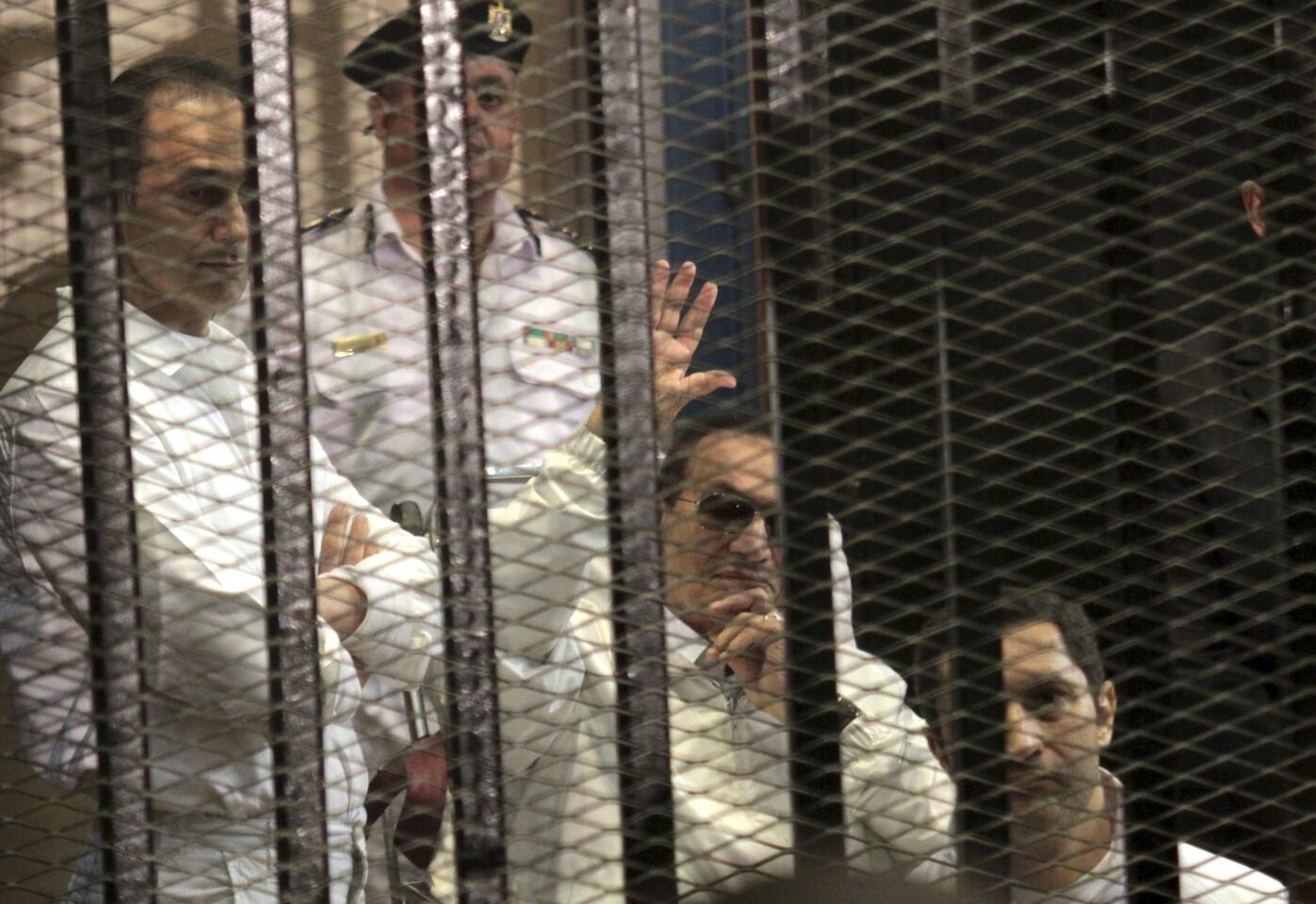 Former Egyptian President Hosni Mubarak, center, waves to supporters in a Cairo courtroom. He and sons Gamal, left, and Alaa attend a hearing in their retrial on appeal.