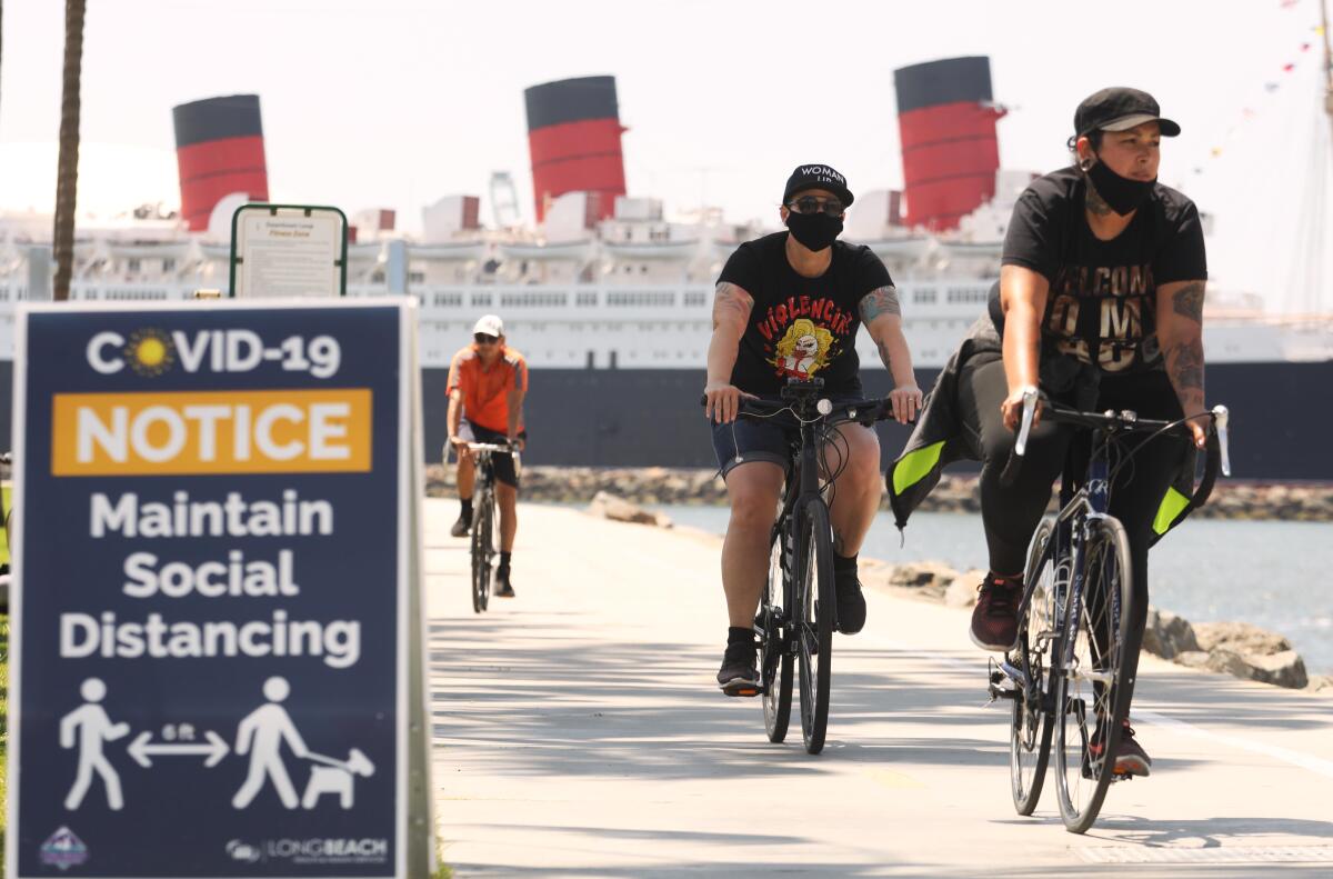 Bikers, against a backdrop of the Queen Mary, make their way along a pedestrian and beach bike path on the first day that Long Beach reopened it.