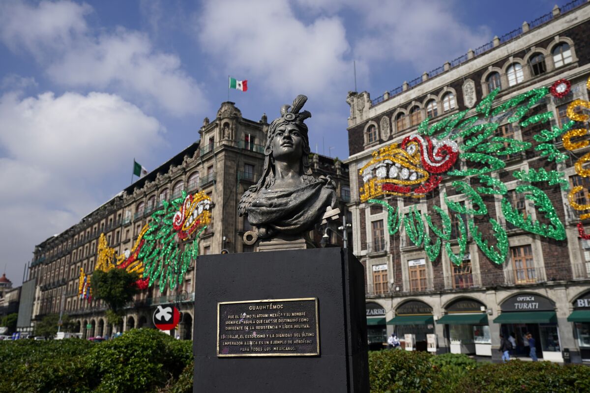 A bust of Aztec emperor Cuauhtemoc in Mexico City's main square with images of Aztec god Quetzalcoatl on nearby buildings.