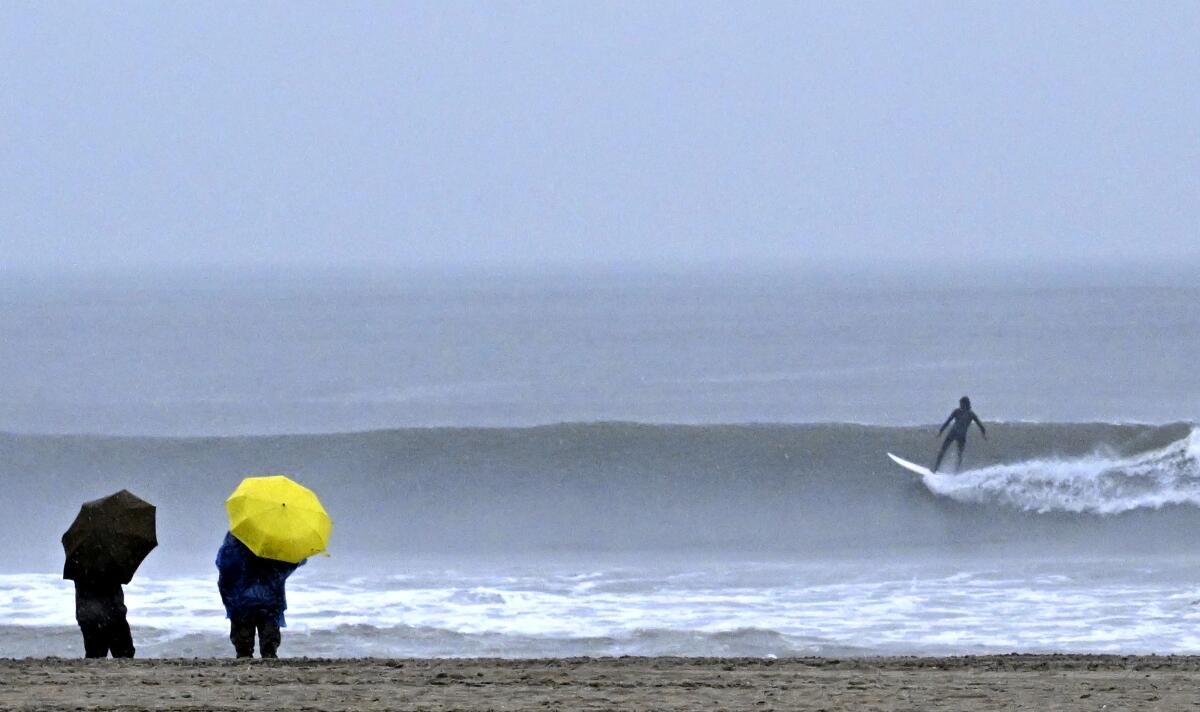 Unas personas caminan junto al mar mientras surfistas montan las olas durante una tormenta en Venice Beach