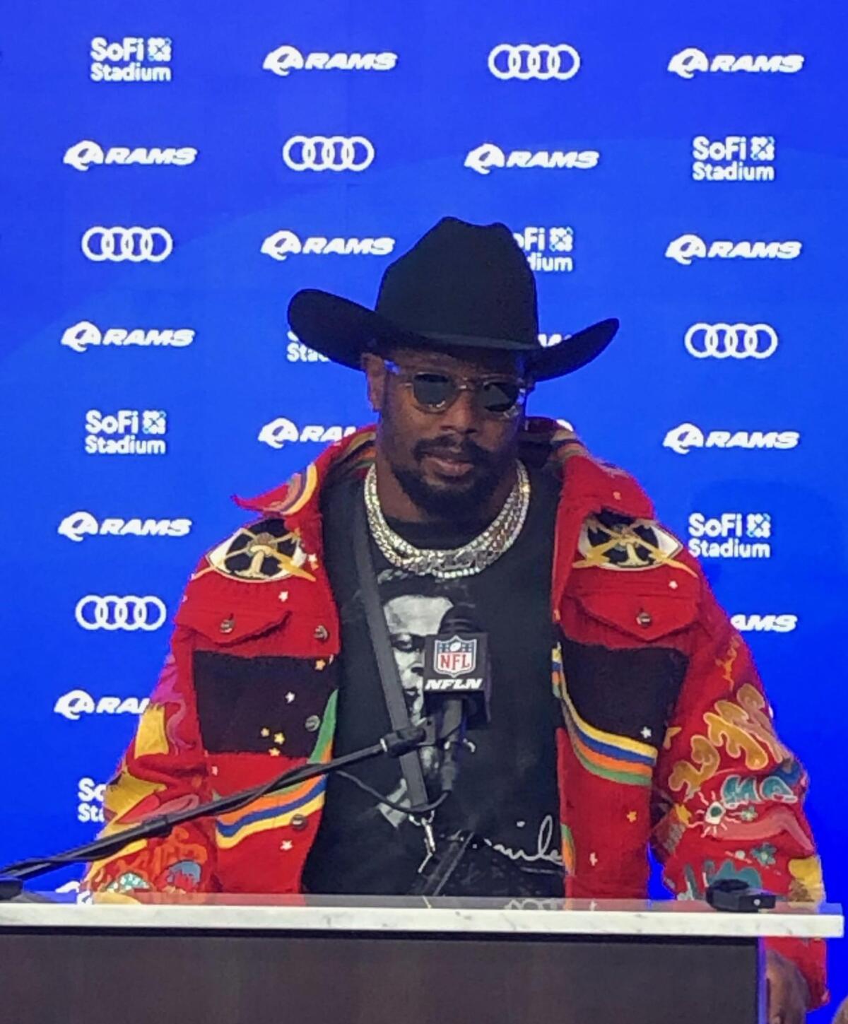 Von Miller stands on a podium wearing a flashy outfit that includes a cowboy hat, multicolored jacket and sunglasses