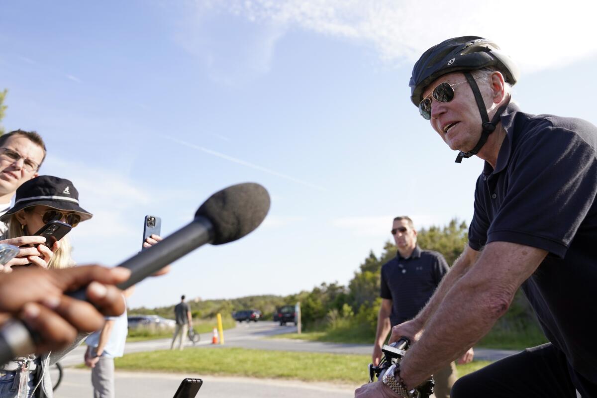 Biden speaks into a microphone while on a bike