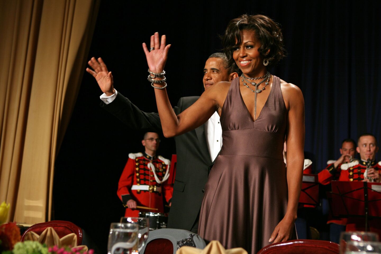 First Lady Michelle Obama is dressed in elegant American style at the 2009 White House correspondents dinner in a mauve-chocolate empire-waist gown accessorized by multiple bracelets and necklaces. She wears her hair in flattering loose curls.