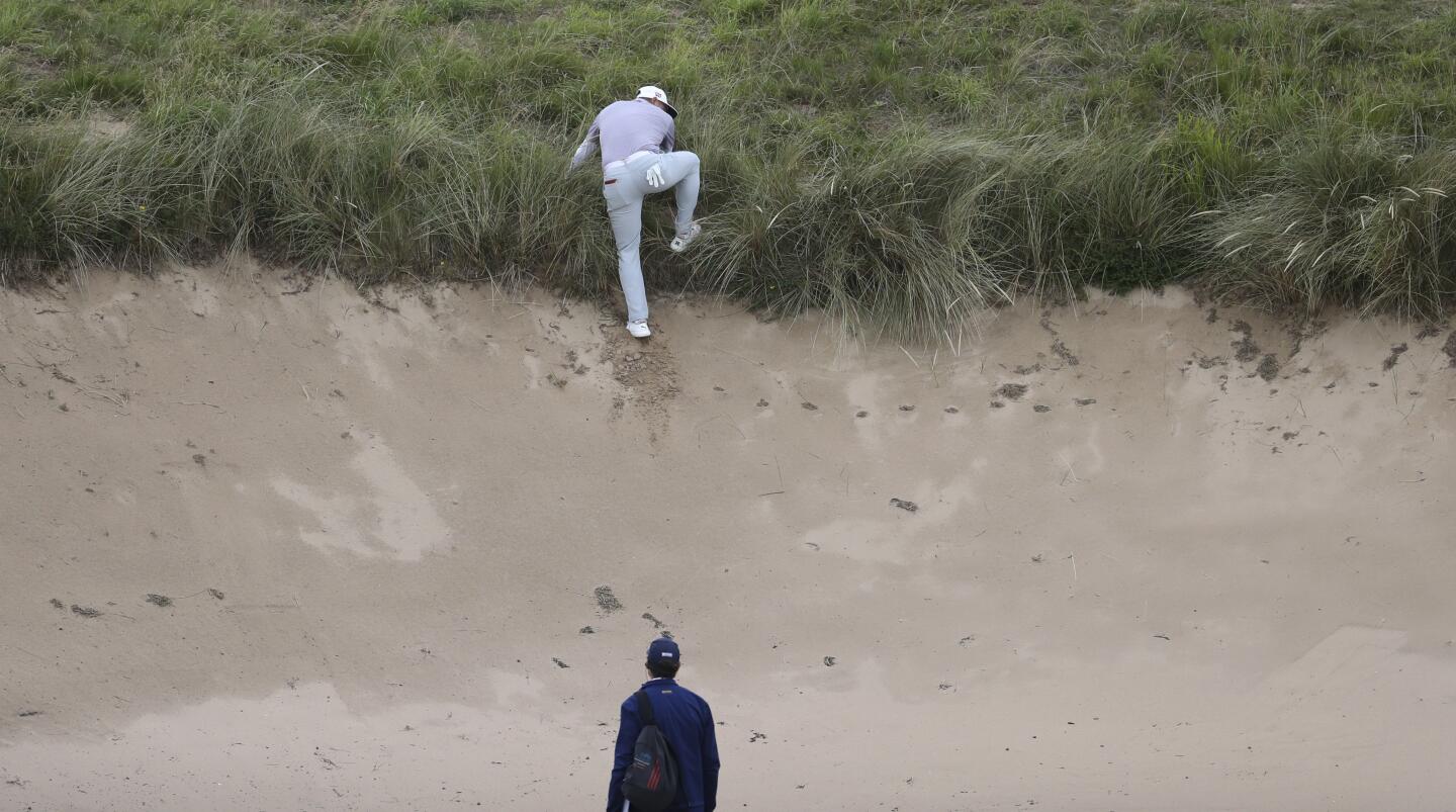 Gary Woodland of the United States climbs the steep wall of a bunker while attempting to find sure footing to play his ball on the top edge of the bunker on the seventh hole during the first round of the 148th Open Championship at Royal Portrush Golf Club in Northern Ireland.