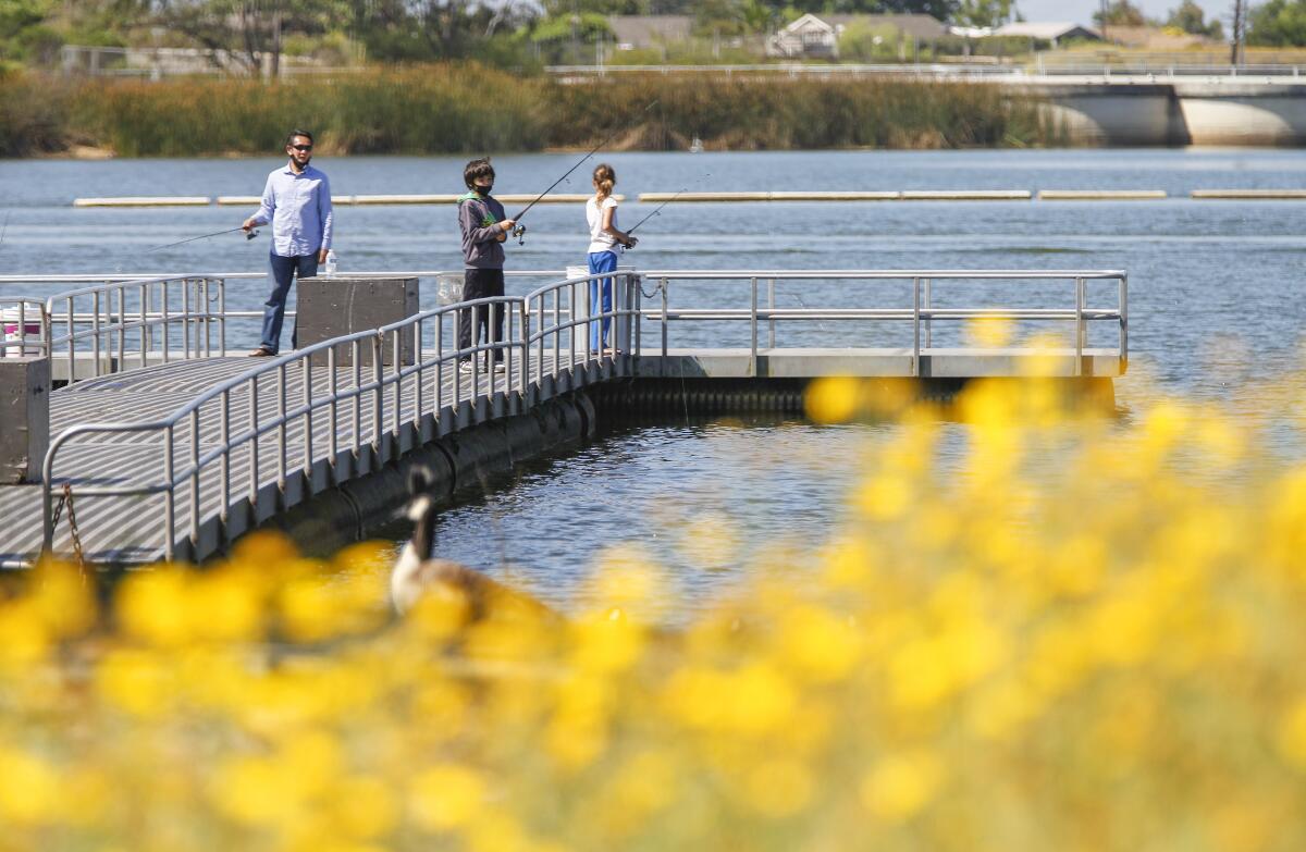 Three people hold fishing rods as they fish off a pier in a reservoir