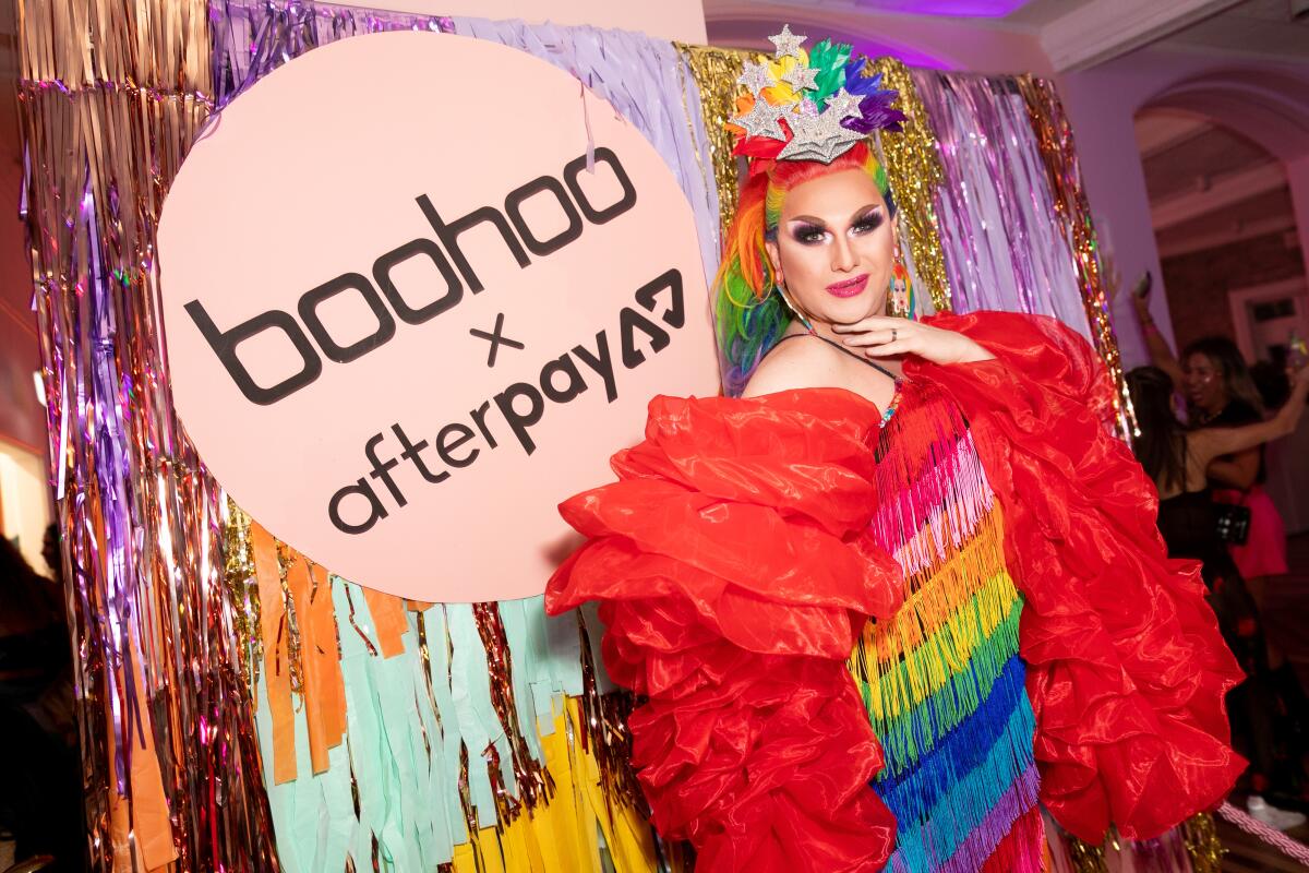 A colorfully dressed young woman stands in front of a sign that say Boohoo x Afterpay 