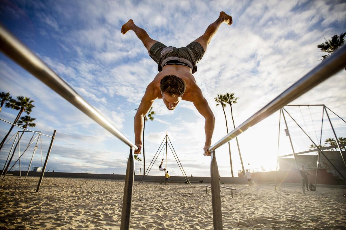A man does a handstand on workout bars at Muscle Beach.