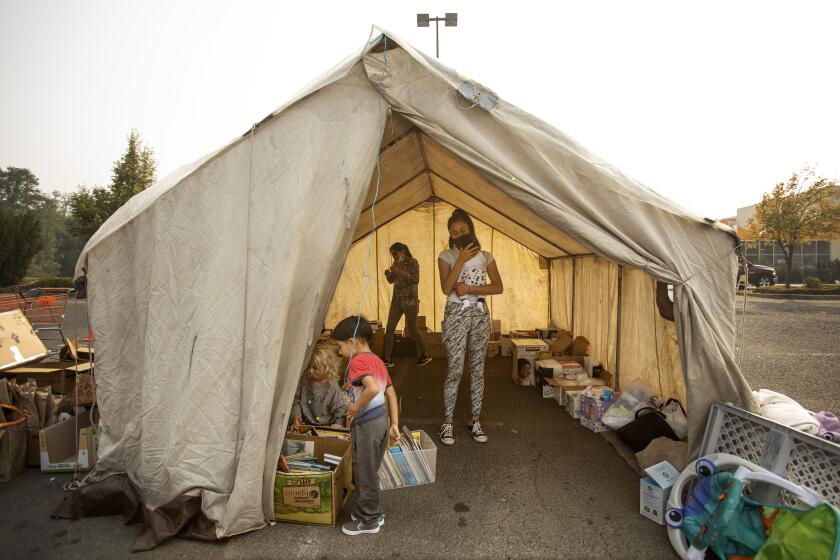 PHOENIX, OR: September 17, 2020 - Mariela Reyes, age 13, holds her baby brother, Kevin, 1 month, as her family collects things at the donation center started and run by staff and faculty of the Phoenix-Talent school district, at the Home Depot in Phoenix. Reyes' family lost their home in Talent. (Katie Falkenberg for the Times)