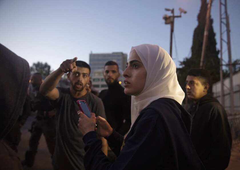 Palestinian activist Muna al-Kurd, center, stands with other activists as Israeli police approach their friends repairing a mural that was defaced by a Jewish settler, in the Sheikh Jarrah neighborhood of east Jerusalem, where Palestinian families face imminent eviction from their homes by Israeli settlers, Monday, May 24, 2021. On Sunday, June 6, 2021, Israel arrested and later released al-Kurd in the contested Sheikh Jarrah neighborhood of Jerusalem, a day after forcefully detaining a prominent journalist there. (AP Photo/Maya Alleruzzo)