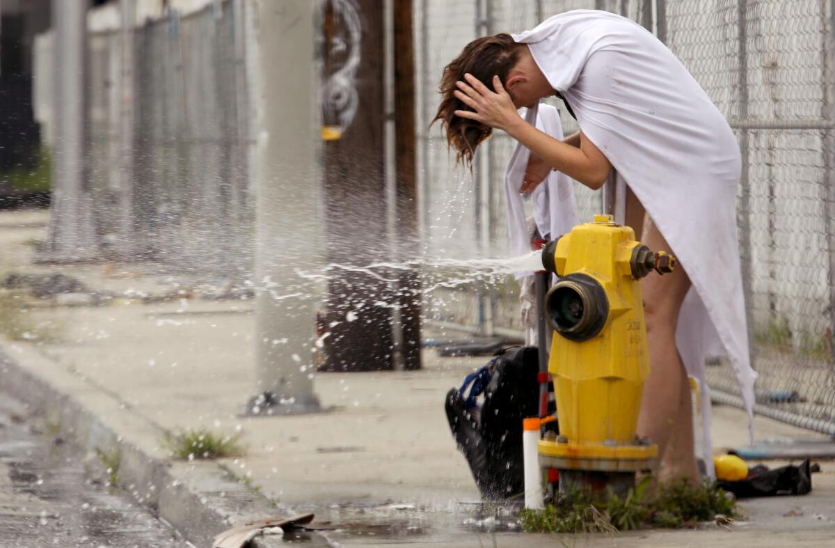 A woman bows her head above a fire hydrant spewing water.