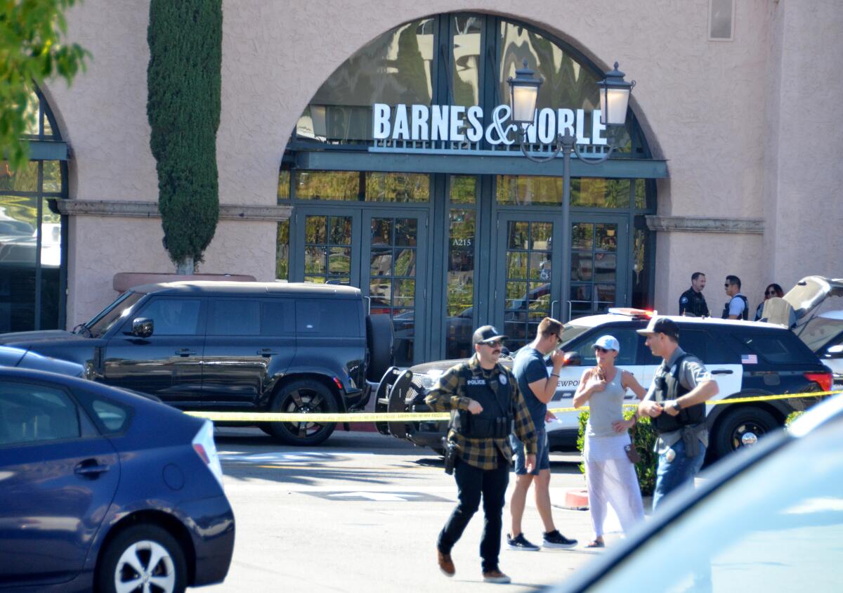 Two people in street clothes and several officers  near yellow crime scene tape outside a Barnes & Noble entrance to a mall