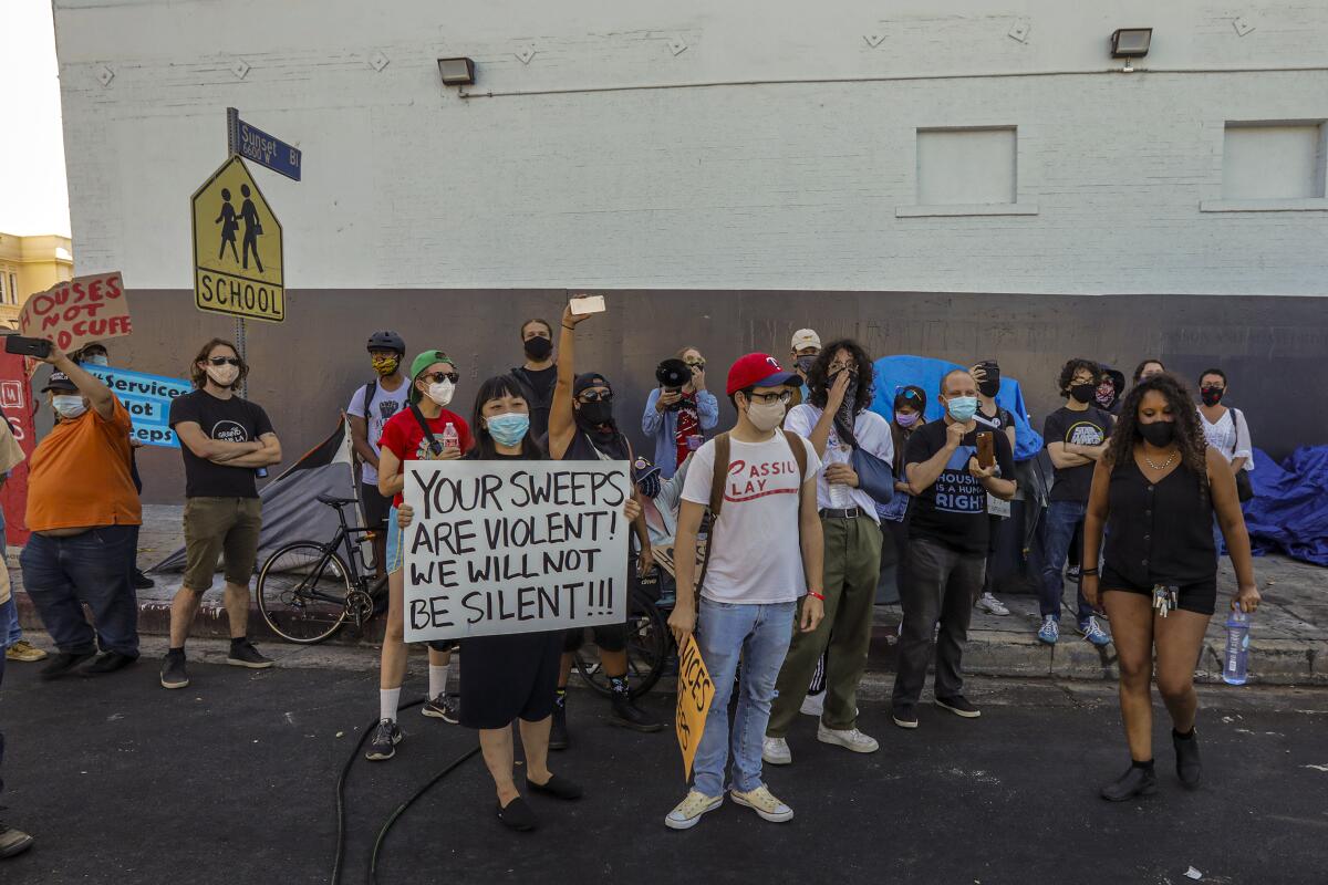 Masked protesters surround sidewalk tents to stop city workers from removing them during a cleanup in Hollywood