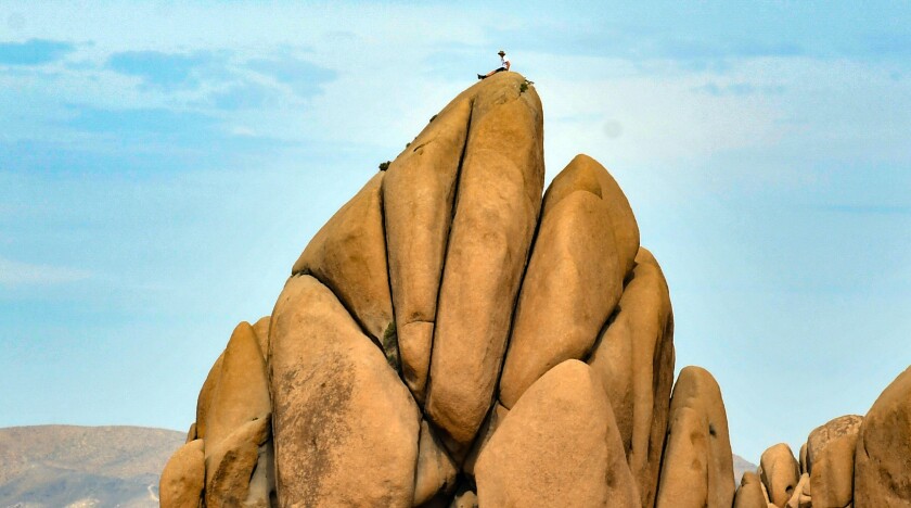 A seated climber looks tiny on top of huge boulders.