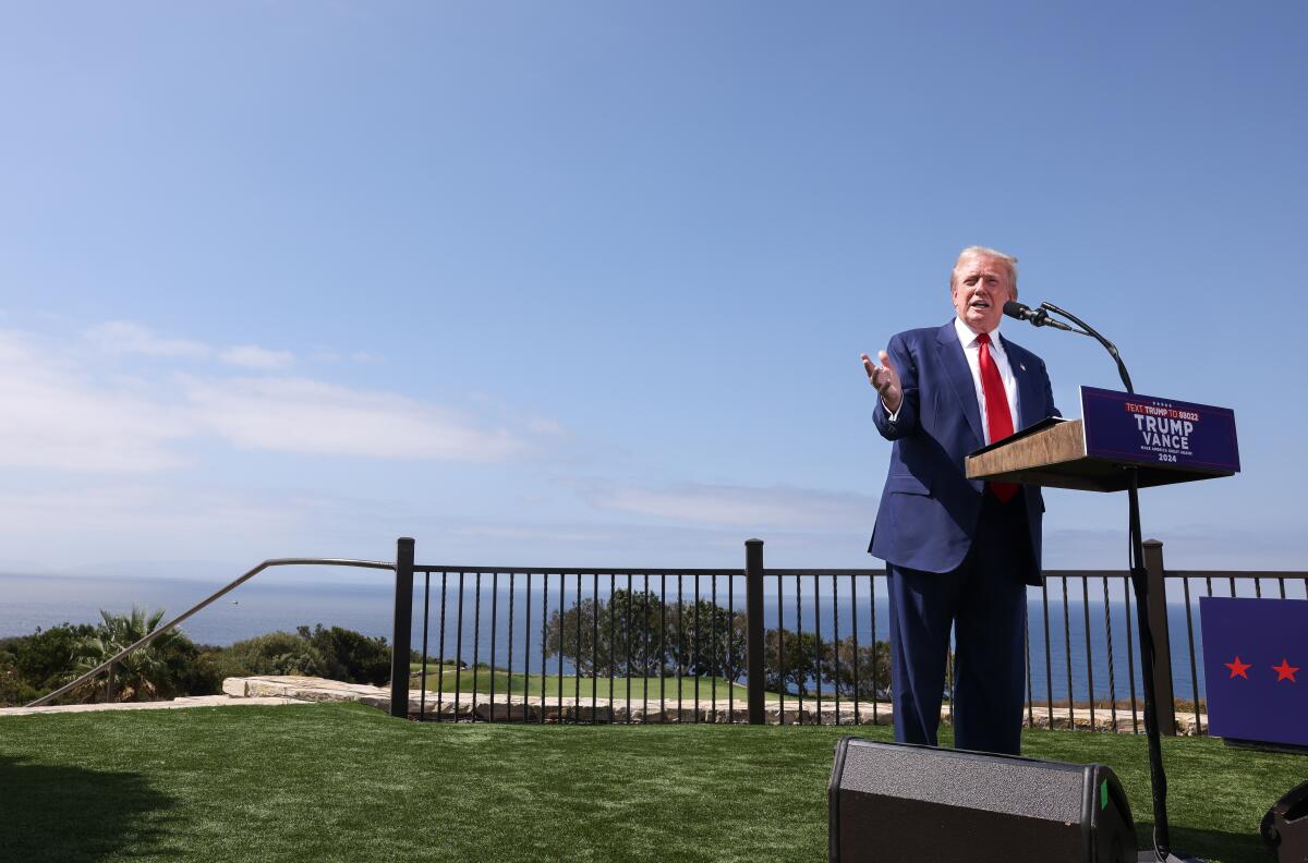 Donald Trump speaks into a microphone in front of the ocean 