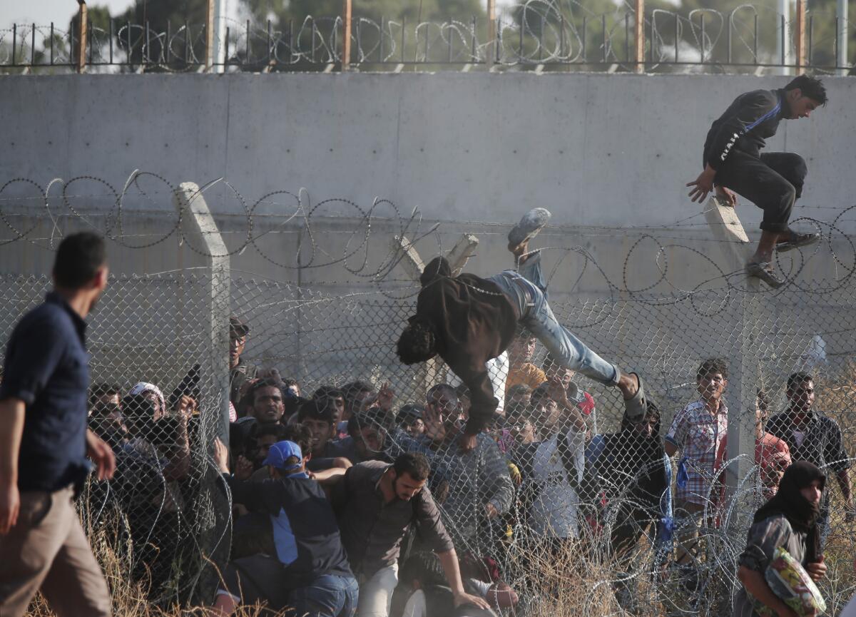 Syrian refugees clamber over a fence to get into Turkey in June.