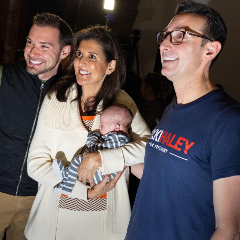 Nikki Haley poses for a photo holding a baby and standing between two men