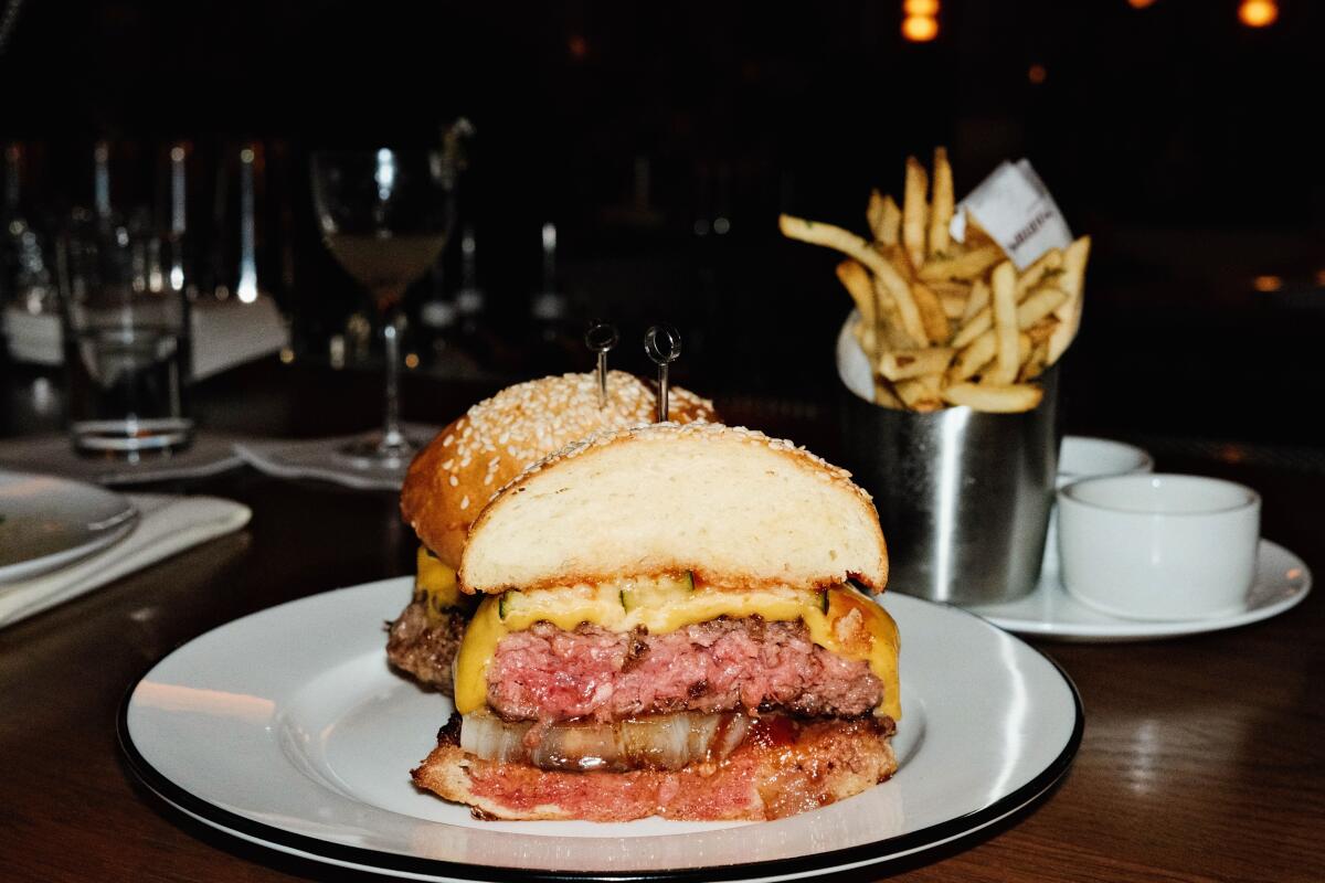 The cheeseburger at the Benjamin, cut in half, on a white plate. French fries are seen in the background.