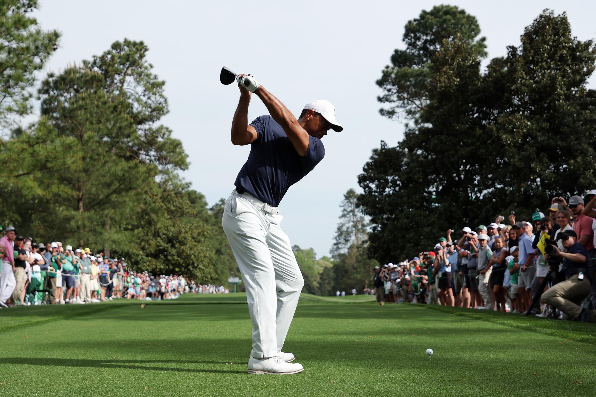 Tiger Woods swings a gold club as people watch