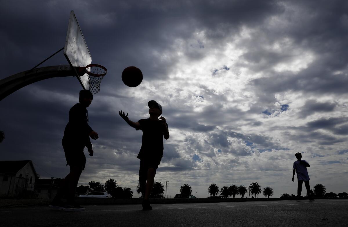 Kids play basketball below cloudy skies.