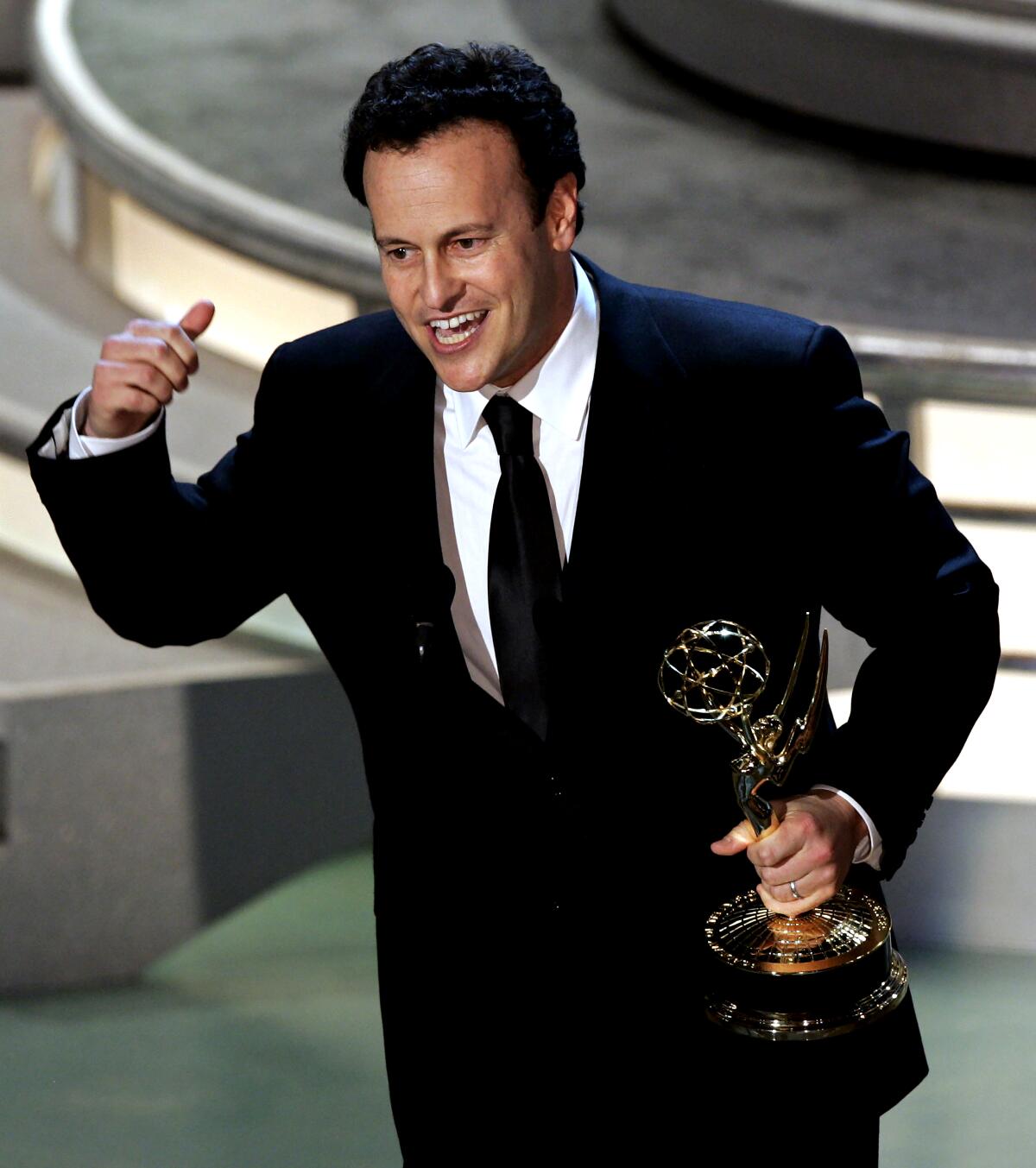 A man gestures while onstage holding an Emmy Award.