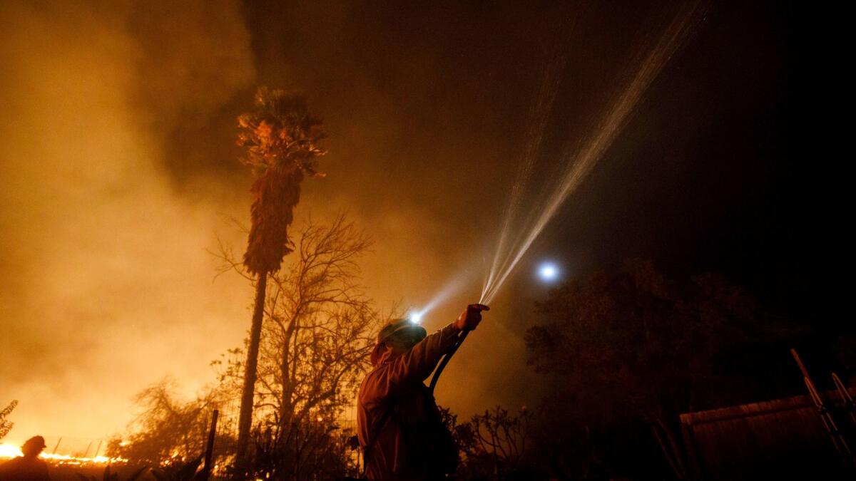 A firefighter uses a garden hose to spray water on rooftop embers while working to save a home from the Lilac fire in San Diego County in December.