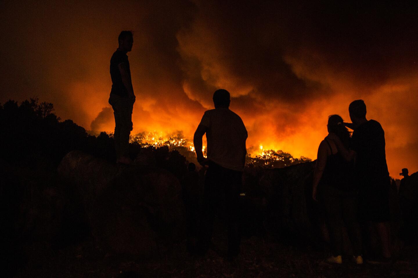 People stand next to the fire before being evacuated at the village of Monchique, in southern Portugal's Algarve region, Sunday, Aug. 5 2018.
